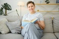 Middle-aged housewife sitting on sofa with book, free time retirement, hobby. Royalty Free Stock Photo