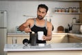 Middle aged Indian man preparing protein shake by adding scoop of powder at kitchen after workout - concept of diet