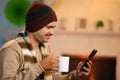 Middle aged Indian man with warmth winter wear using mobile phone by drinking tea at home - concept of relaxation