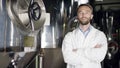 A middle-aged labouring man in a white overall standing near the factory equipment and smiling into a camera. A front