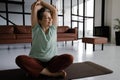 A middle aged lady practices yoga at home. A smiling woman with closed eyes in bliss sits on a mat on the floor in the