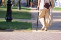 Invalid woman navigates sidewalk with cane and shopping bag