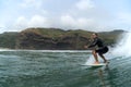 A middle aged male surfer in a black wetsuit rides a wave with cliffs, coastal hills and a blue cloudy sky in the background at