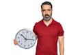 Middle aged man with beard holding big clock thinking attitude and sober expression looking self confident Royalty Free Stock Photo