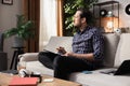 A middle-aged man with a beard is sitting on a couch with an English dictionary in his hands. The boy is trying to Royalty Free Stock Photo