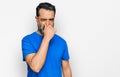 Middle aged man with beard wearing casual blue t shirt smelling something stinky and disgusting, intolerable smell, holding breath Royalty Free Stock Photo