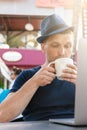 A middle-aged man in a blue hat is drinking coffee in front of a laptop. portrait close-up, looking into a mug. vertical photo