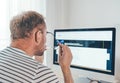 A middle-aged man checking a vision in eyeglasses in front of the modern computer. Home office, distance, or freelance work on