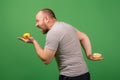 A middle-aged man chooses apple versus brownie on a green background. The concept of choosing the right healthy food Royalty Free Stock Photo