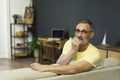 Middle-aged man covering mouth with hand and round eyes, wearing round eyeglasses, experiencing deep astonishment and fear indoor