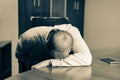  Ill man at desk in office, feeling sick, depressed and exhausted. He is just sitting at working place with his head on the table.