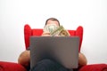 Middle-aged man in glasses with a laptop on his lap sitting in a red chair and counting money Royalty Free Stock Photo