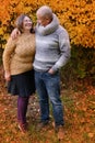 Middle-aged man in a gray sweater and a woman in a yellow stand, embracing, in an autumn park against the background of trees, the Royalty Free Stock Photo