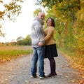 Middle-aged man in a gray sweater and a woman in a yellow stand, embracing, in an autumn park against the background of trees, the Royalty Free Stock Photo