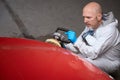 Middle-aged man is grinding damaged section of red car body