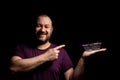 A middle-aged man in his forties holds a toy grocery basket in his hand against a black background and points with a finger to an Royalty Free Stock Photo