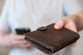 A middle-aged man is holding an old purse. Brown leather wallet in a man`s hand. Middle section of a mature man in a gray T-shirt Royalty Free Stock Photo