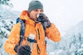 Middle-aged Man with a hot drink cup and a thermos flask dressed bright orange softshell jacket drinking while he trekking winter Royalty Free Stock Photo