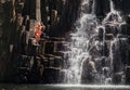 Middle-aged man jumping in waterfall lake. Falling water streams flow on black volcanic stone cascades. Rochester Falls waterfall