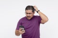 A middle aged man looking confounded and stumped, scratching his head while looking at his cellphone. Wearing eyeglasses and a Royalty Free Stock Photo