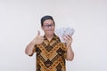 A middle aged man making a thumbs up sign while holding a lot of cash in his hand, flaunting his wealth or earnings.