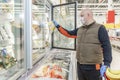 A middle-aged man in a medical mask and gloves chooses frozen foods in a supermarket refrigerator. Healthy eating during the Royalty Free Stock Photo