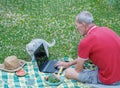 middle aged man with mobile phone and laptop lies on a blanket in green grass Royalty Free Stock Photo