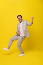 Middle aged man pretend playing guitar laughing wearing white suit isolated on yellow background. Handsome mature Royalty Free Stock Photo