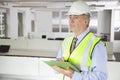 Middle-aged man in reflector vest and hard hat with clipboard at office