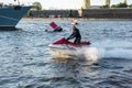 A middle-aged man rides a jet ski on the Neva River in the center of St. Petersburg. Warships on the background. Sunny day. Summer