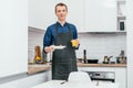 Middle-aged man with short ginger hair in blue shirt, black apron stand holding glass of orange juice and white plate. Royalty Free Stock Photo