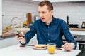 Middle-aged man with short ginger hair in blue shirt looking at mobile phone thunderstruck with news with arm raised.