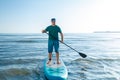 A middle-aged man in shorts and a T-shirt stands on a SUP board with a paddle near the sea. Royalty Free Stock Photo