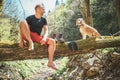Middle-aged man sitting on the fallen tree log over the mountain forest stream and Smiling to beagle dog while he waiting for Royalty Free Stock Photo