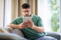 Middle-aged man sitting at home on the sofa and holding digital tablet in his hand Royalty Free Stock Photo