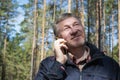 A middle-aged man smiles and talks on the phone in the park