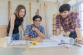 Middle aged man wearing blue plaid shirt holding pencil explaining and discussing blueprint document to young male and female Royalty Free Stock Photo