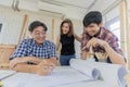 Middle aged man wearing blue plaid shirt holding pencil explaining and discussing blueprint document to young male and female Royalty Free Stock Photo