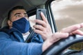 Middle-aged man wearing mask, using cell phone and distracted while driving a car frightened by the accident about to occur on the Royalty Free Stock Photo