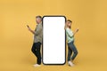 Middle aged man and woman using smartphones, leaning on large phone with empty screen, advertising website, mockup Royalty Free Stock Photo