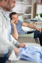 middle aged man ironing while friend on sofa Royalty Free Stock Photo