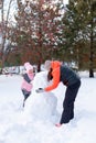 Middle aged mother and little cute daughter standing on snow making snowman together on backyard in evening with rowan Royalty Free Stock Photo
