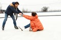 Middle-aged positive couple skating on open air ice rink. Man helping fallen woman to get up. Concept of leisure