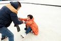 Middle-aged positive couple skating on open air ice rink. Man helping fallen woman to get up. Concept of leisure