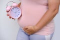Middle-aged pregnant woman holds alarm clock near her belly close-up, waiting for newborn, concept of prenatal contractions, Royalty Free Stock Photo