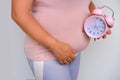 middle-aged pregnant woman holds alarm clock near her belly close-up, waiting for newborn, concept of prenatal contractions,