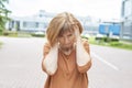 A middle-aged redhead woman in casual clothes stands on the street covering her ears with her hands. Royalty Free Stock Photo