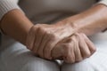 Middle aged senior woman holding wrinkled hands on lap.