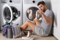 Middle aged single man with laundry basket and dirty clothes near washing machine at home. Millennial man putting Royalty Free Stock Photo