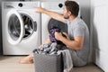 Middle aged single man with laundry basket and dirty clothes near washing machine at home. Millennial man putting Royalty Free Stock Photo